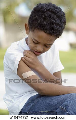 Boy (7-9) examining bandaid on arm, outdoors View Large Photo Image Stock Image - Boy (7-9) examining bandaid on arm, outdoors. Fotosearch