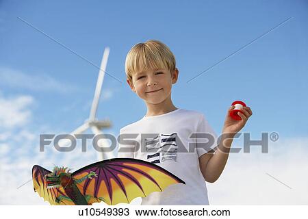 Stock Image - Boy (7-9) holding kite at wind farm, portrait. Fotosearch