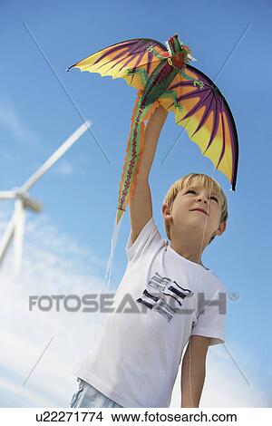Picture - Boy (7-9) playing with kite at wind farm. Fotosearch