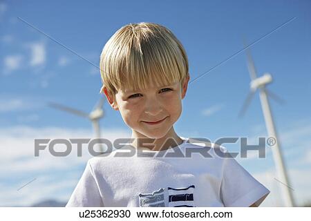 Stock Image - Boy (7-9) smiling at wind farm, portrait. Fotosearch