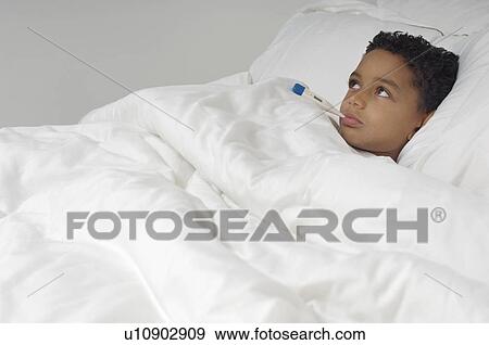 Stock Photo - Boy (7-9) with thermometer in mouth, lying in bed. Fotosearch