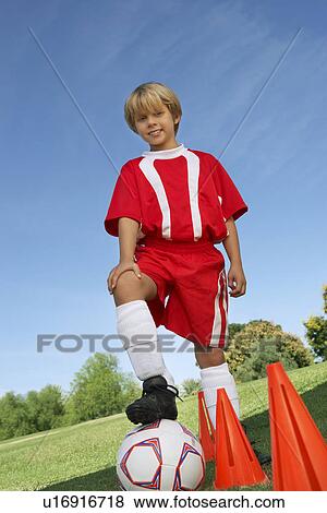 Stock Photo - Boy (7-9 years) soccer player holding foot on ball, portrait. Fotosearch