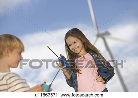 Stock Image - Boy and girl (5-9) playing with walky-talkies at wind farm. Fotosearch