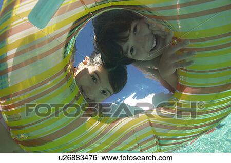 Stock Photograph - Boy and girl looking through inflatable raft in swimming pool, underwater view. Fotosearch