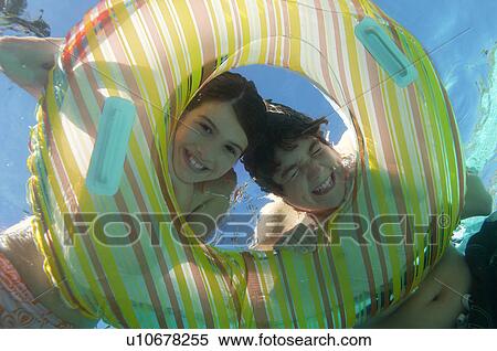 Stock Photography - Boy and girl looking through inflatable raft in swimming pool, underwater view. Fotosearch