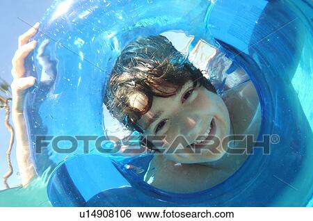 Stock Photograph - Boy looking through inflatable raft in swimming pool, underwater view. Fotosearch