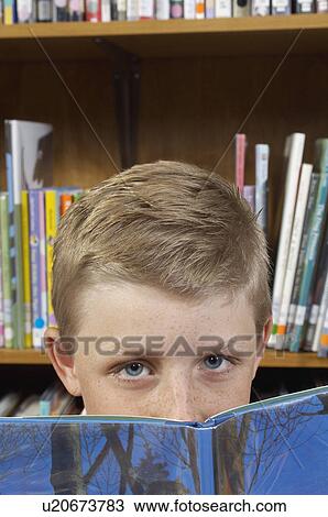 Stock Image - Boy peeking above book, close-up view. Fotosearch