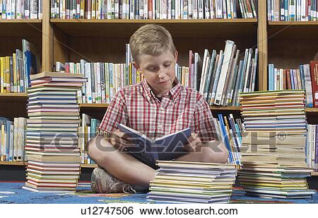 Boy sitting on the floor and reading book in library View Large Photo Image Stock Photograph - Boy sitting on the floor and reading book in library. Fotosearch