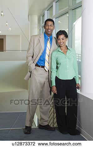 Stock Image - Business couple standing in office building, portrait. Fotosearch