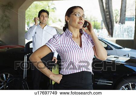 Business couple using mobile phones near car View Large Photo Image Stock Photo - Business couple using mobile phones near car. Fotosearch