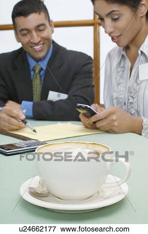 Stock Photo - Business man and woman at cafe, focus on cappuccino in foreground. Fotosearch