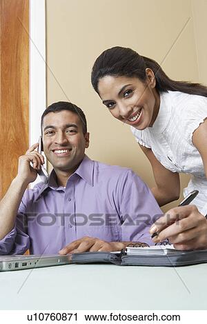Stock Image - Business man and woman working at desk in office, portrait. Fotosearch
