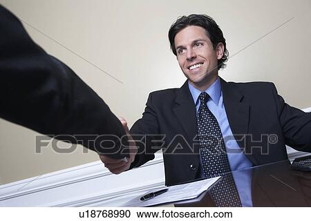 Business man shaking hands with colleague at desk in office View Large Photo Image Stock Image - Business man shaking hands with colleague at desk in office. Fotosearch
