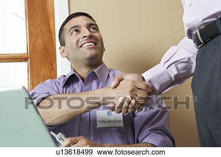 Stock Photo - Business man shaking hands with colleague at desk in office. Fotosearch