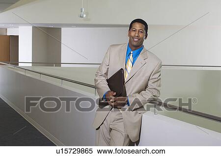 Stock Photography - Business man standing by balustrade in office building, portrait. Fotosearch