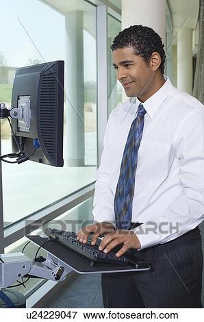 Business man using internet on computer in office hallway View Large Photo Image Stock Photo - Business man using internet on computer in office hallway. Fotosearch