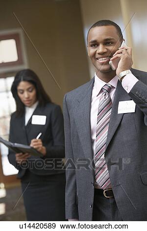 Business man using mobile phone with business woman writing in diary in background View Large Photo Image Stock Photo - Business man using mobile phone with business woman writing in diary in background. Fotosearch