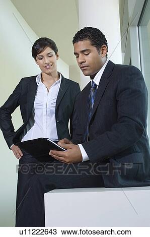 Stock Image - Business man writing in hallway with business woman. Fotosearch