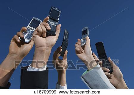Stock Photo - Business people holding mobile phones up in air, close-up of hands. Fotosearch