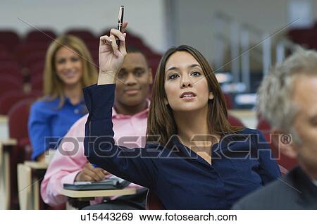Stock Photo - Business people sitting in auditorium, woman rising hand. Fotosearch