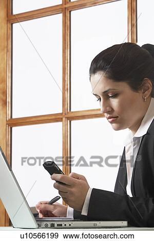 Stock Photo - Business woman text messaging using mobile phone in office. Fotosearch