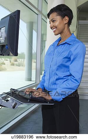 Stock Photograph - Business woman using internet on computer in office hallway. Fotosearch