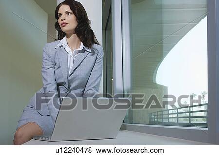 Business woman using laptop sitting on window ledge View Large Photo Image Stock Photo - Business woman using laptop sitting on window ledge. Fotosearch