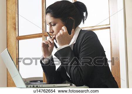 Picture - Business woman using mobile phone at desk in office. Fotosearch