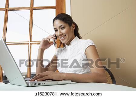Stock Image - Business woman using mobile phone at desk in office, portrait. Fotosearch