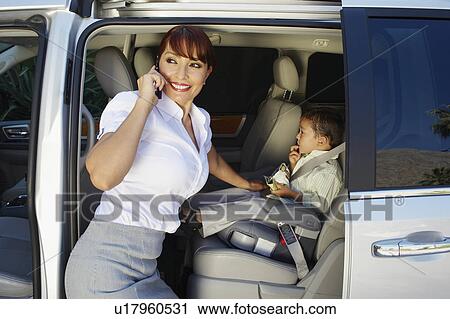 Stock Image - Business woman using mobile phone with son in car. Fotosearch