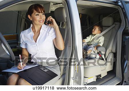 Stock Photo - Business woman using mobile phone with son in car. Fotosearch