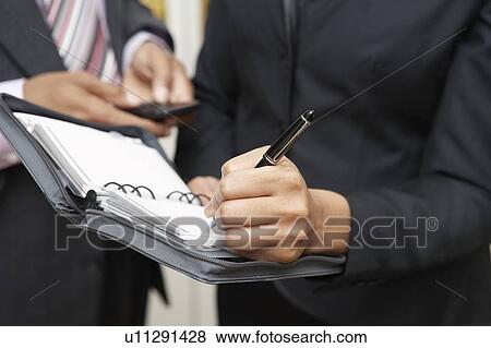 Stock Photo - Business woman writing in diary, mid section. Fotosearch