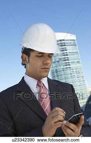 Stock Image - Businessman in hardhat using PDA outdoors. Fotosearch