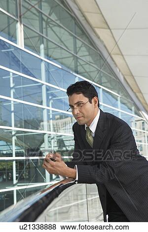 Stock Photo - Businessman leaning on railing outside office building. Fotosearch
