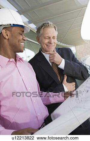 Businessman looking at blueprints with construction worker View Large Photo Image Stock Image - Businessman looking at blueprints with construction worker. Fotosearch