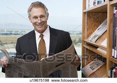 Businessman reading newspaper library, portrait View Large Photo Image Stock Photo - Businessman reading newspaper library, portrait. Fotosearch
