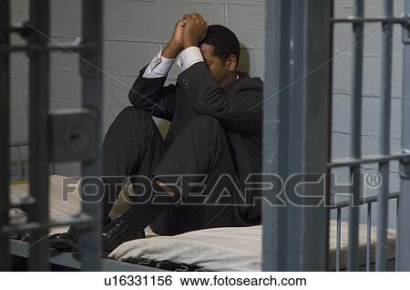 Stock Photograph - Businessman sitting on bed in prison cell. Fotosearch