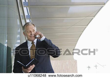 Businessman using cell phone holding day planner View Large Photo Image Stock Photo - Businessman using cell phone holding day planner. Fotosearch