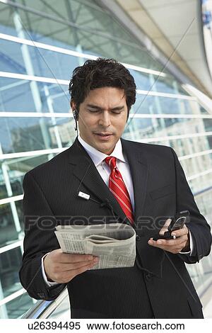 Businessman using mobile phone, reading newspaper outside office building View Large Photo Image Stock Photography - Businessman using mobile phone, reading newspaper outside office building. Fotosearch