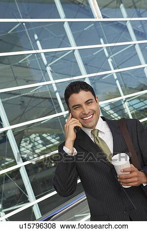 Businessman using mobile phone with take away coffee outside office building View Large Photo Image Stock Photo - Businessman using mobile phone with take away coffee outside office building. Fotosearch