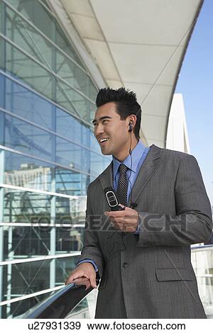 Stock Photo - Businessman using mobile phone with earpiece office building. Fotosearch