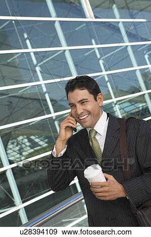 Businessman using mobile phone with take away coffee outside office building View Large Photo Image Stock Photo - Businessman using mobile phone with take away coffee outside office building. Fotosearch