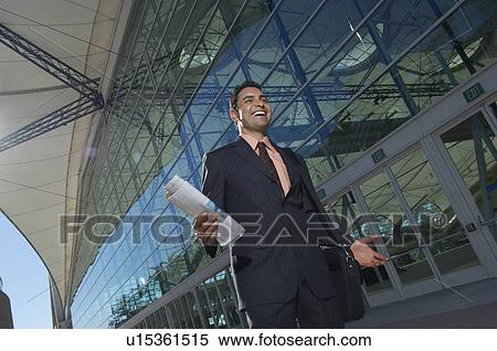 Stock Photography - Businessman walking outside office building and smiling, low angle view. Fotosearch