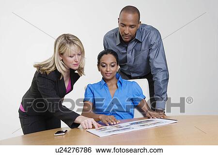 Stock Photograph - Businesspeople Looking at Booklet in Meeting. Fotosearch