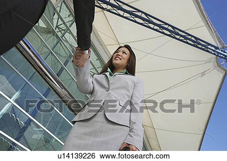 Stock Photograph - Businesswoman shaking hands with businessman outdoors, low angle view. Fotosearch