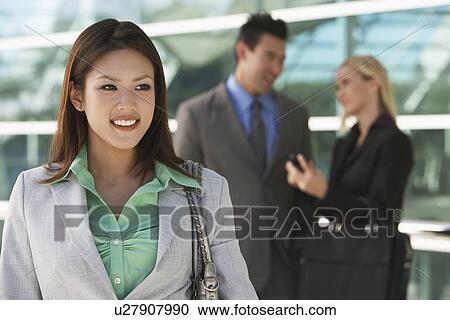 Stock Image - Businesswoman smiling with colleagues in background, outdoors. Fotosearch