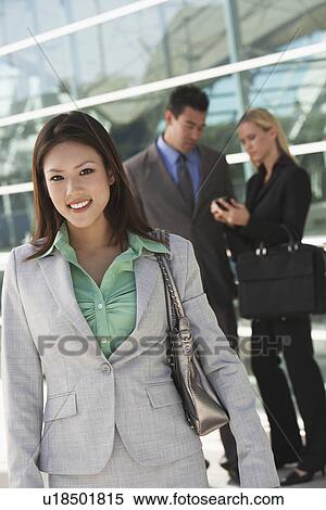 Businesswoman smiling with colleagues in background, outdoors View Large Photo Image Stock Photography - Businesswoman smiling with colleagues in background, outdoors. Fotosearch