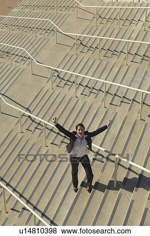 Stock Photo - Businesswoman standing on stairs and yelling with arms raised, elevated view. Fotosearch