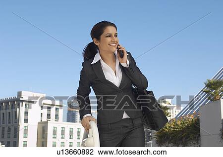 Stock Image - Businesswoman talking on mobile phone outdoors. Fotosearch