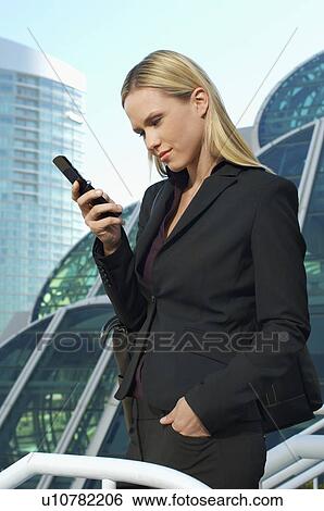 Stock Photograph - Businesswoman text messaging outside office building. Fotosearch